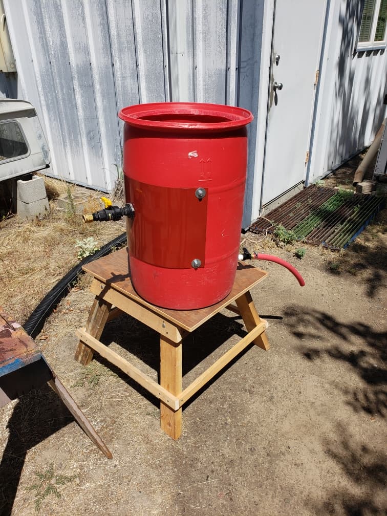 A red 30 gallon drum rinse station on a wooden stand outside the shop, hoses attached